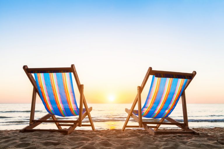 Two deck chairs on a tropical sandy beach with beautiful colorful sunset